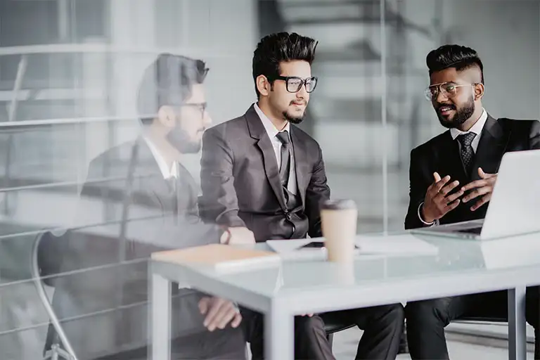 Three indian businessmen sitting around table meeting in modern open plan office